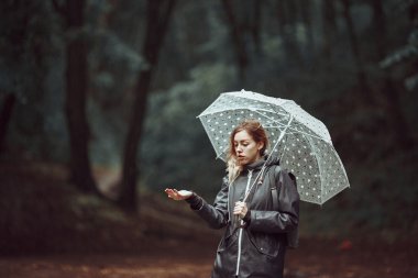 Genç kız şemsiye ile yağmurlu bir ormanda yürürken. 