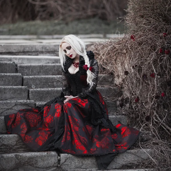 Mulher bonita wBeautiful mulher com cabelo loiro longo em vestido vermelho old fashioned andando através de mortos garden.ith longo cabelo loiro no vestido vermelho old fashioned — Fotografia de Stock