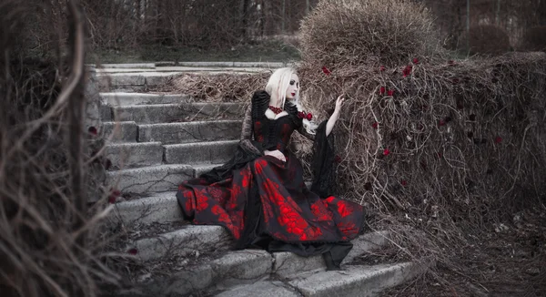 Hermosa mujer wBeautiful mujer con el pelo largo y rubio en vestido rojo pasado de moda caminando a través de muertos garden.ith pelo largo y rubio en vestido rojo pasado de moda — Foto de Stock