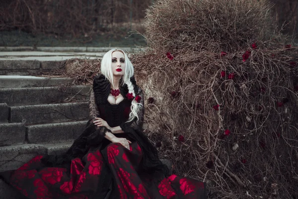 Hermosa mujer wBeautiful mujer con el pelo largo y rubio en vestido rojo pasado de moda caminando a través de muertos garden.ith pelo largo y rubio en vestido rojo pasado de moda —  Fotos de Stock