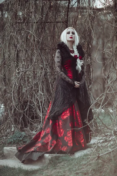 Hermosa mujer wBeautiful mujer con el pelo largo y rubio en vestido rojo pasado de moda caminando a través de muertos garden.ith pelo largo y rubio en vestido rojo pasado de moda —  Fotos de Stock