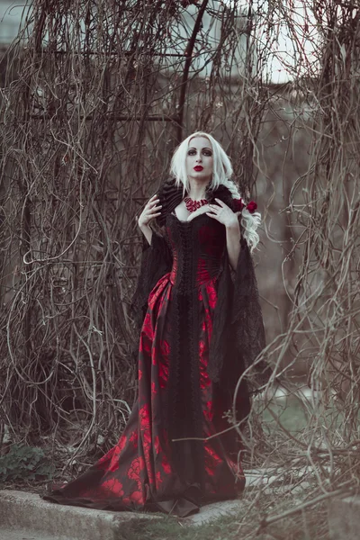 Hermosa mujer wBeautiful mujer con el pelo largo y rubio en vestido rojo pasado de moda caminando a través de muertos garden.ith pelo largo y rubio en vestido rojo pasado de moda —  Fotos de Stock