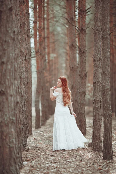 Chica pelirroja en vestido blanco caminando en el bosque de pinos . — Foto de Stock