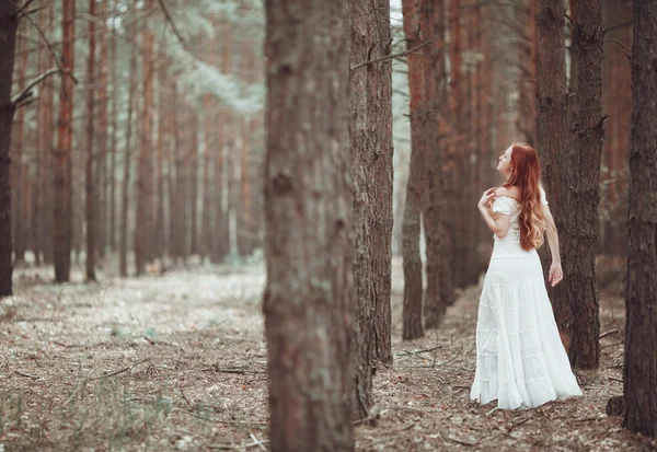 Gember meisje in witte jurk wandelen in bos. — Stockfoto