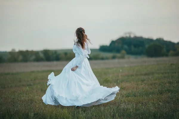 Menina em vestido vintage branco andando através do campo de primavera . — Fotografia de Stock