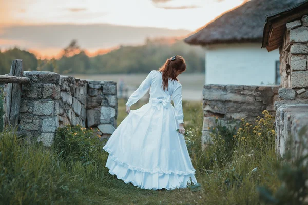 Schönes Mädchen in weißem Vintage-Kleid, das in der Nähe eines alten Steinhauses spaziert. Vintage-Brautkonzept — Stockfoto