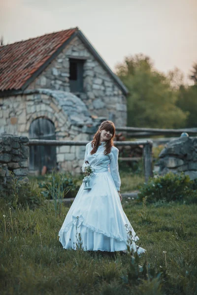 Bella ragazza in abito bianco vintage a piedi vicino a casa di pietra antica. Concetto di sposa vintage — Foto Stock