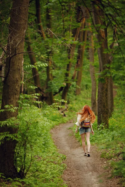 Молодая рыжая девушка идет через свежий зеленый лес. Концепция туризма . — стоковое фото