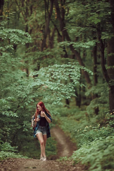 Young redhead girl walking through fresh green forest. Tourism concept. — Stock Photo, Image