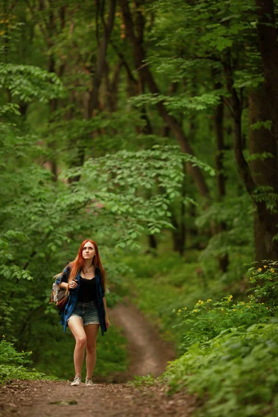 Молодая рыжая девушка идет через свежий зеленый лес. Концепция туризма . — стоковое фото