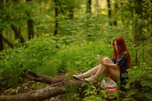 Chica sentada en un árbol con su celular en el bosque. Concepto Gadget. Concepto de viaje . —  Fotos de Stock