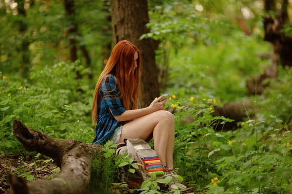 Chica sentada en un árbol con su celular en el bosque. Concepto Gadget. Concepto de viaje . —  Fotos de Stock