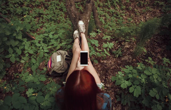 Girl sitting on a tree with her cell phone in the forest. Gadget concept. Travel concept. — Stock Photo, Image