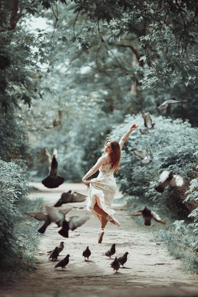 Chica joven en hermoso vestido y zapatos puntiagudos bailando en la calle con palomas voladoras . — Foto de Stock