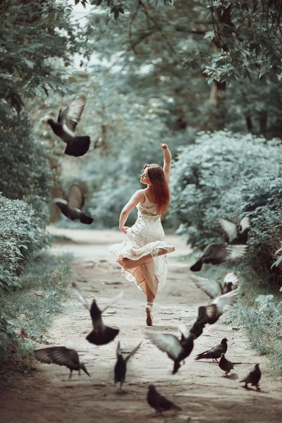 Jong meisje in een mooie jurk en pointe-schoenen dansen op straat met vliegende duiven. — Stockfoto