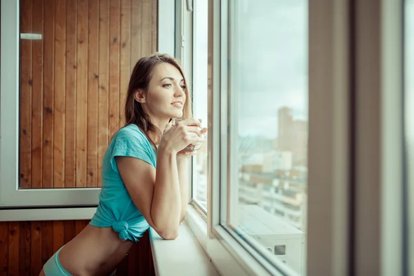 Yong girl with cup of tea standing on the balcony in the morning. Royalty Free Stock Images