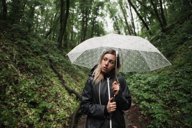 Genç kız şemsiye ile yağmurlu bir ormanda yürürken. 