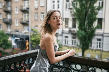 Sırtı açık saten elbise enjoyng balkonunda yağmur güzel genç kız.