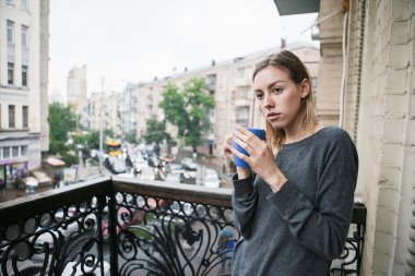 Yağmurda balkonda duran sabah kahvesi ile güzel genç kız. Düşünme kavramı. 