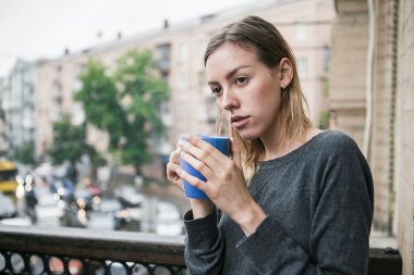 Yağmurda balkonda duran sabah kahvesi ile güzel genç kız. Düşünme kavramı. 