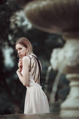 Güzel genç kız moda pembe elbise ayakta vintage taş çeşme yakınındaki.