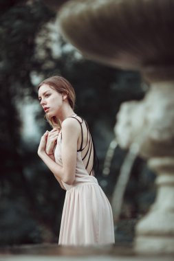 Güzel genç kız moda pembe elbise ayakta vintage taş çeşme yakınındaki.
