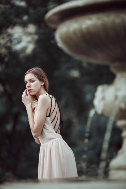 Güzel genç kız moda pembe elbise ayakta vintage taş çeşme yakınındaki.