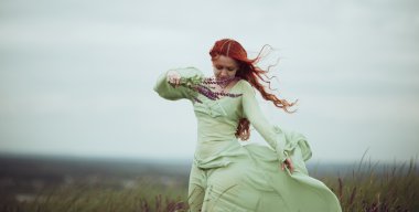 Adaçayı çiçekleri olan alana yürürken Ortaçağ elbiseli genç Kızıl saçlı kız. Rüzgar kavramı. Fantezi