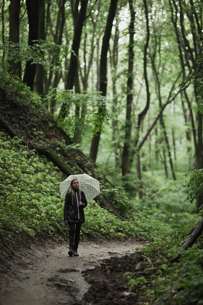 Chica joven caminando a través de un bosque lluvioso con paraguas . —  Fotos de Stock