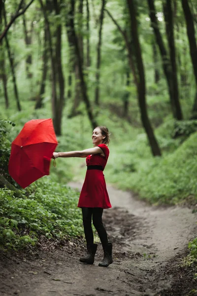 Chica feliz en vestido rojo caminando en el bosque verde fresco con paraguas. Concepto de lluvia . —  Fotos de Stock