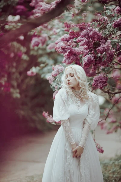 Beautiful blonde woman in blooming lilac garden. Vintage bride concept — Stock Photo, Image