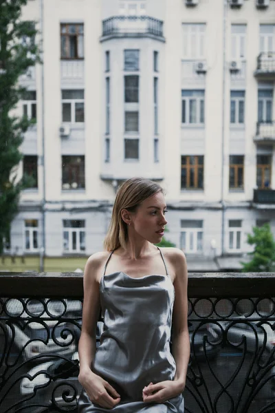 Mooi jong meisje in backless satijnen jurk enjoyng de regen op het balkon. — Stockfoto