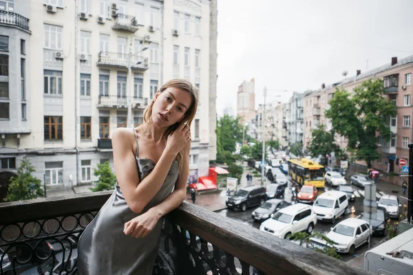 Hermosa chica joven en vestido de satén sin espalda enjoyng la lluvia en el balcón . —  Fotos de Stock