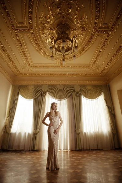 Красива дівчина в довгій сукні, що летить в золотому бароковому інтер'єрі . — стокове фото