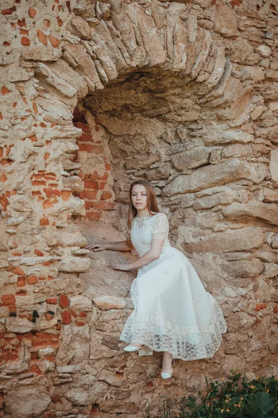 Beautiful young girl in white vintage dress walking near ancient castle. — Stock Photo, Image