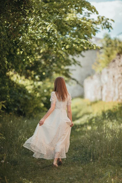 Hermosa joven en vestido vintage blanco caminando cerca del antiguo castillo . — Foto de Stock