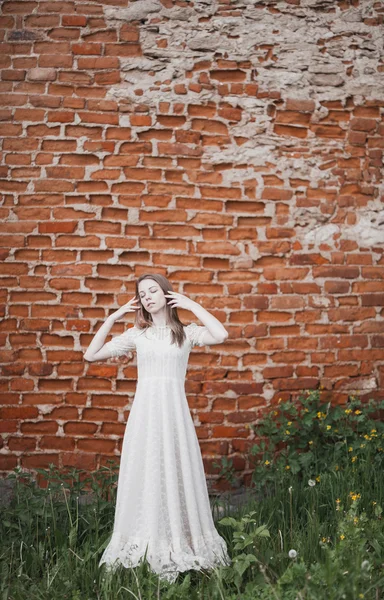 Hermosa joven en vestido vintage blanco de pie cerca de la pared de ladrillo viejo — Foto de Stock