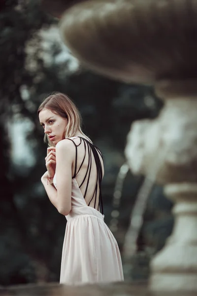 Menina bonita em vestido rosa na moda em pé perto de fonte de pedra vintage . — Fotografia de Stock