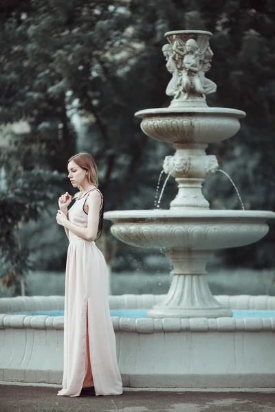Bella ragazza in abito rosa alla moda in piedi vicino fontana di pietra vintage . — Foto Stock
