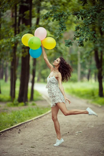 Mooi jong meisje, plezier in het park van de zomer met gekleurde ballonnen. Happy glimlach sprong concept — Stockfoto