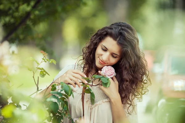 Mooi meisje ruikt roze roos in de lentetuin — Stockfoto