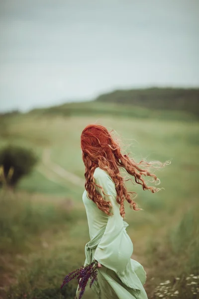 Menina ruiva jovem em vestido medieval andando através do campo com flores de sálvia. Conceito de vento. Fantasia — Fotografia de Stock