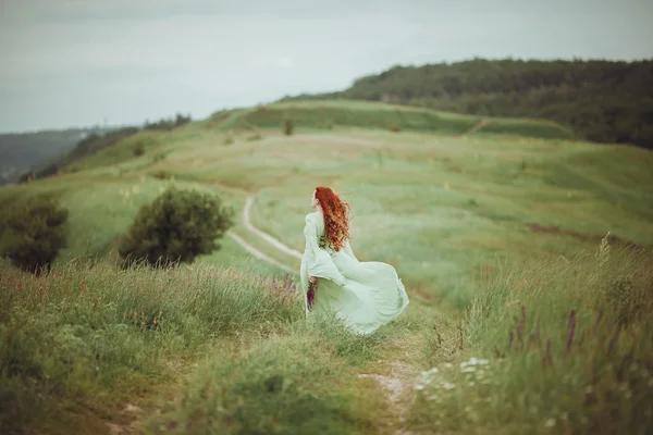 Jeune fille rousse en robe médiévale marchant à travers le champ avec des fleurs de sauge. Concept de vent. Fantaisie — Photo