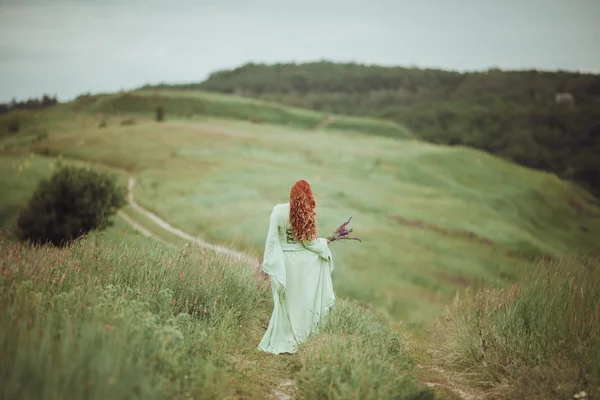 Fiatal vöröshajú lány séta mező zsálya virágok középkori ruhában. Szél fogalma. Fantasy — Stock Fotó