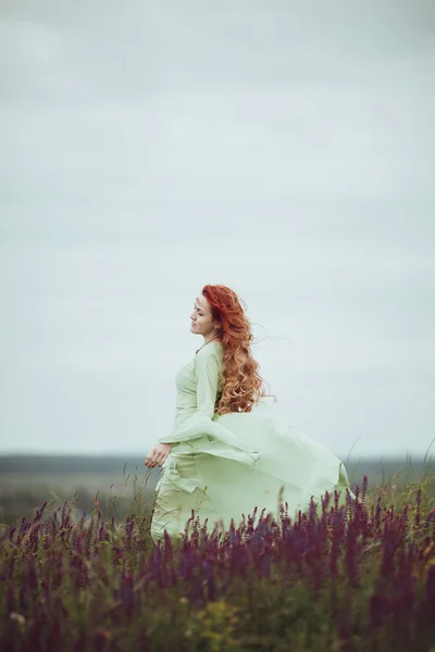 Νέοι κοκκινομάλλα κοπέλα στο μεσαιωνικό φόρεμα περπατώντας πεδίο με φασκόμηλο. Άνεμος έννοια. Φαντασία — Φωτογραφία Αρχείου
