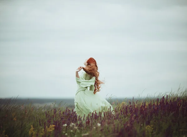 Jeune fille rousse en robe médiévale marchant à travers le champ avec des fleurs de sauge. Concept de vent. Fantaisie — Photo