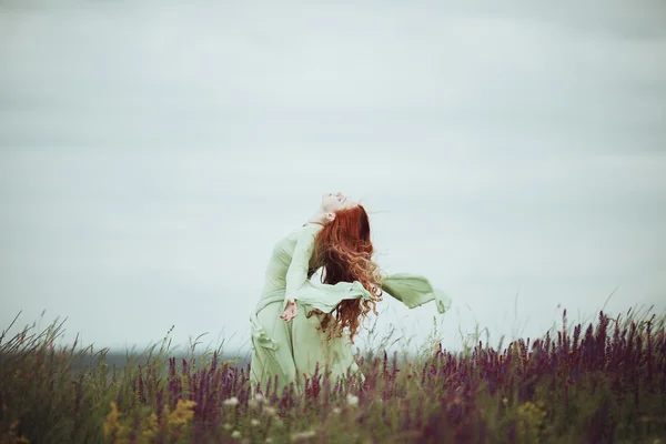 Unga rödhårig flicka i medeltida klänning går genom fältet med salvia blommor. Wind koncept. Fantasy — Stockfoto