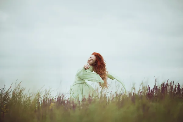 Chica pelirroja joven en vestido medieval caminando por el campo con flores de salvia. Concepto de viento. Fantasía —  Fotos de Stock