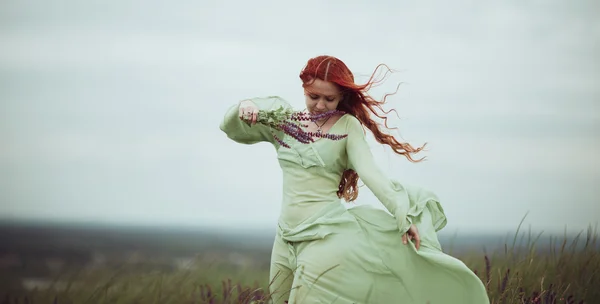Menina ruiva jovem em vestido medieval andando através do campo com flores de sálvia. Conceito de vento. Fantasia — Fotografia de Stock