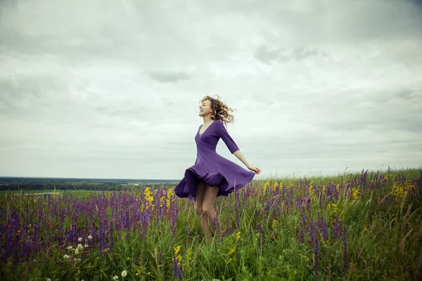 Junges Mädchen im Vintage-Kleid geht durch Salbeiblumenfeld. — Stockfoto